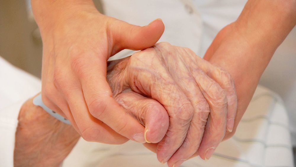 Alte Patientin reicht Pflegerin die Hand